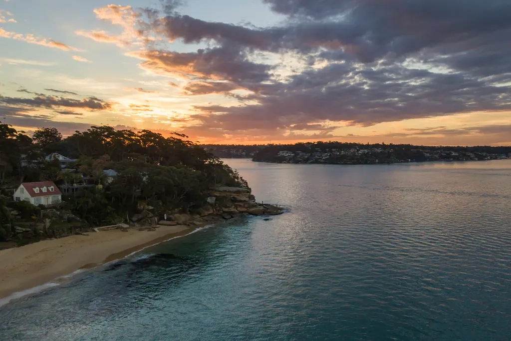 Elevated view over the water at Cronulla in the Sutherland Shire at sunset, with a sandy beach and a bushland headland