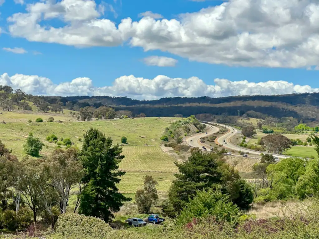The Federal Highway winding through green hills and bushland near Bywong in New South Wales under a blue sky with scattered cloud