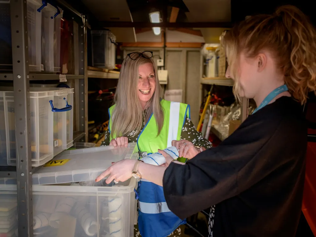 Two people sorting items from clear plastic tubs on storeroom shelving, one wearing a high visibility vest