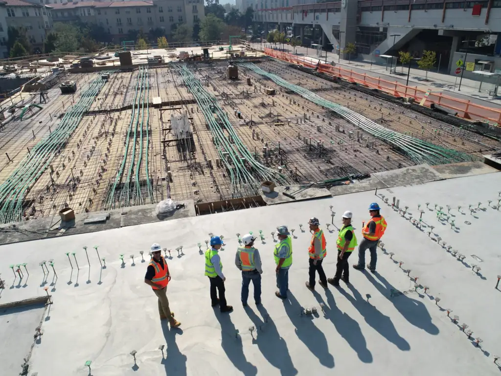 A team of seven workers in hard hats and high visibility vests standing together on a concrete slab on a construction site